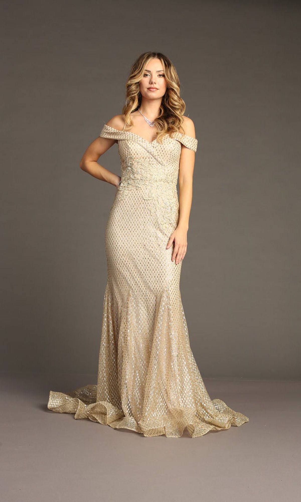 A woman wears the Off-the-Shoulder Long Prom Dress: Chicas DM4024, a mermaid gown embellished with gold sequins, as she poses elegantly against a plain gray background.